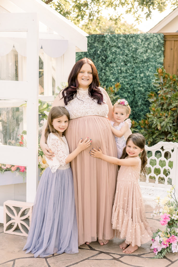 three siblings with their hands on mom's baby bump posing for pictures outside a white greenhouse in McKinney Texas